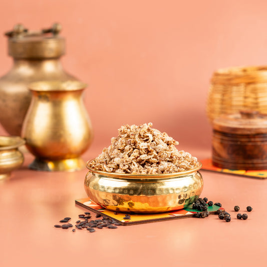 A bowl of air fried red rice spicy snack on a table with golden rice grains spilling out, against a pink background with traditional Indian pottery in the background.