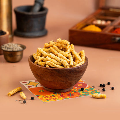 A wooden bowl filled with crispy, peppery rice cakes, presented on a table with spice jars and a colorful fabric underneath.