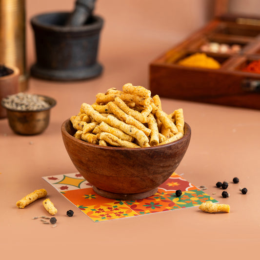 A wooden bowl filled with crispy, peppery rice cakes, presented on a table with spice jars and a colorful fabric underneath.