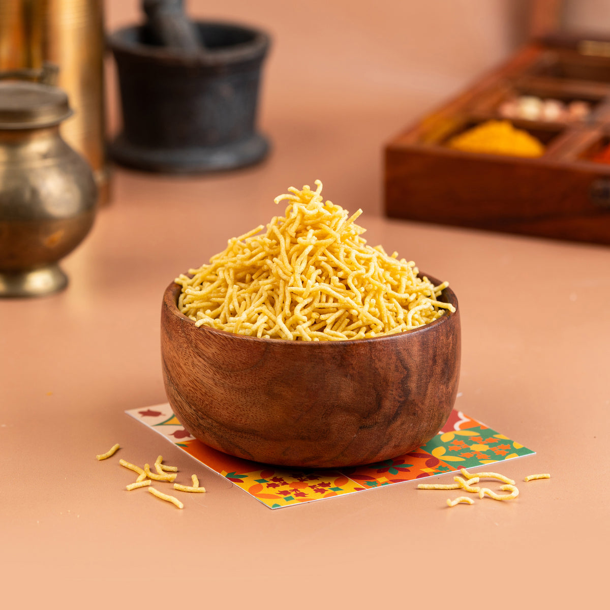 A bowl of Sattur Ompodi (Ajwain) snack on a table with a wooden texture and a colorful cardboard packaging underneath.