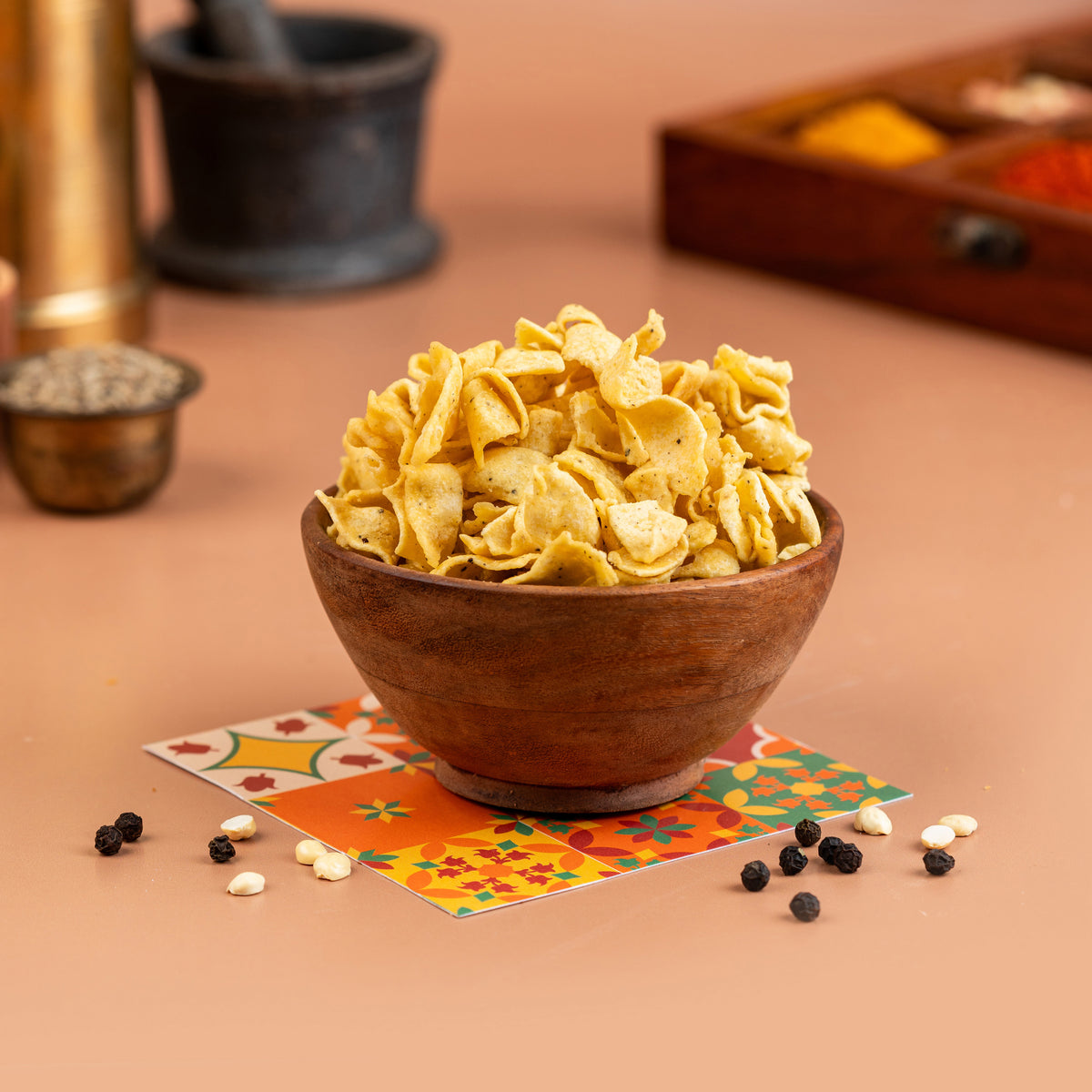 A wooden bowl filled with yellow crispy snacks, placed on a colorful napkin with decorative items in the background.