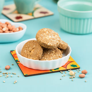 A white bowl filled with sprouted kambu (millet) and peanut cookies on a colorful placemat, with a scattering of peanuts and a blue pot in the background.