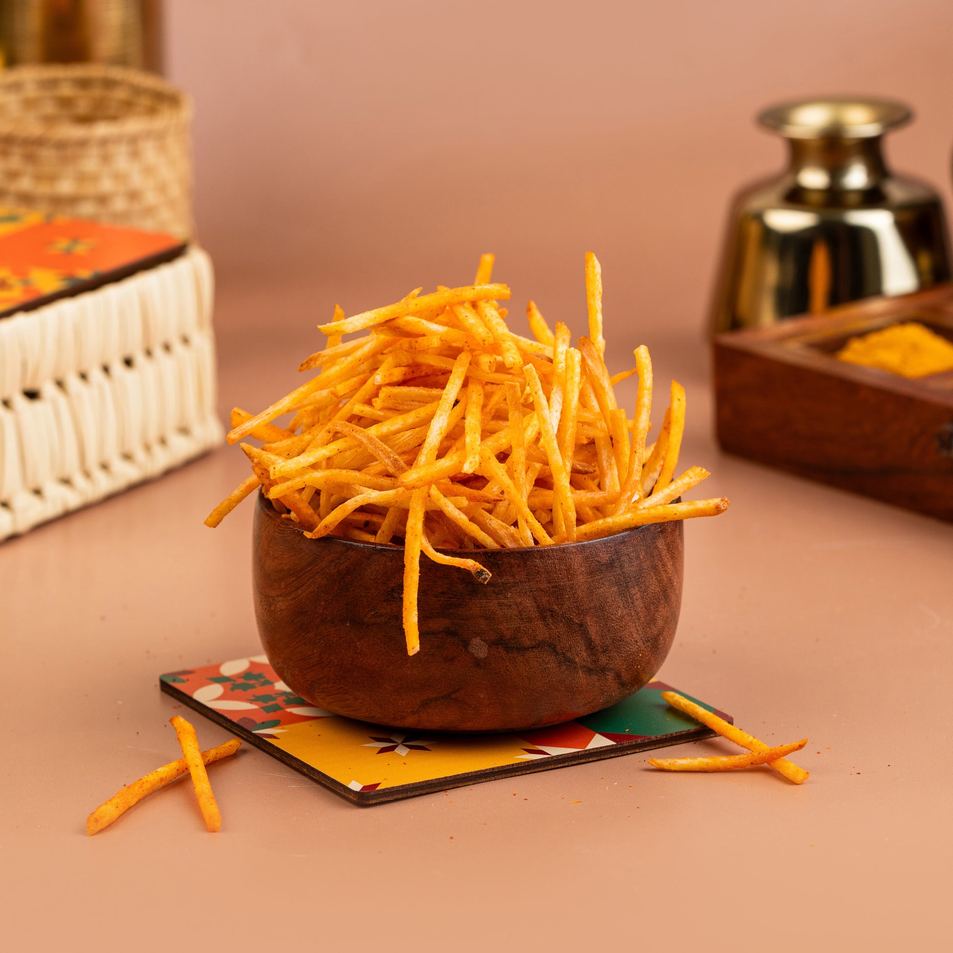 A wooden bowl filled with crispy, seasoned tapioca finger chips on a table, with a blurred background featuring kitchenware.
