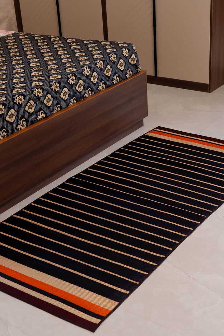 Striped rug on a floor next to a bed with patterned bedding.