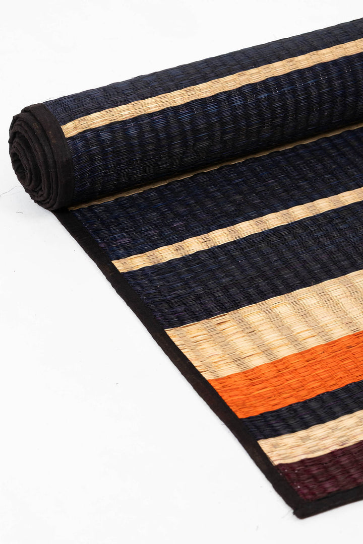 Rolled-up striped rug with black, orange, and beige pattern on a white background