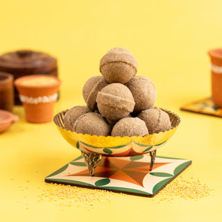 A decorative bowl filled with spherical Foxtail Millet Ghee Ladoo (Thinai Nei Ladoo) on a colorful mat against a yellow background.