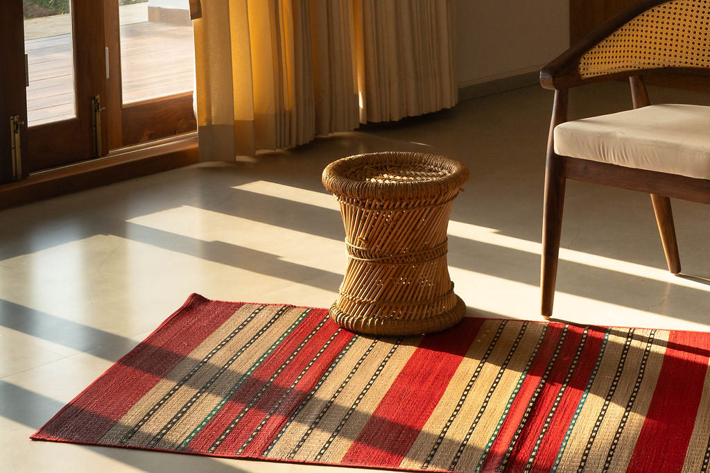 Striped grass mat with a woven stool and chair in a room with sunlight streaming through a window.