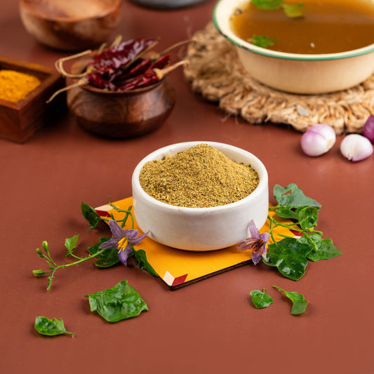 A bowl of Thuthuvalai Soup mix with leafy vegetables, spices, and a touch of herbs, presented on a table with the ingredients and a backdrop of spices.