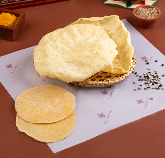 A photo showing freshly prepared Urad Dal Appalam, also known as a Vadagam, displayed on a flat surface with condiments in the background.