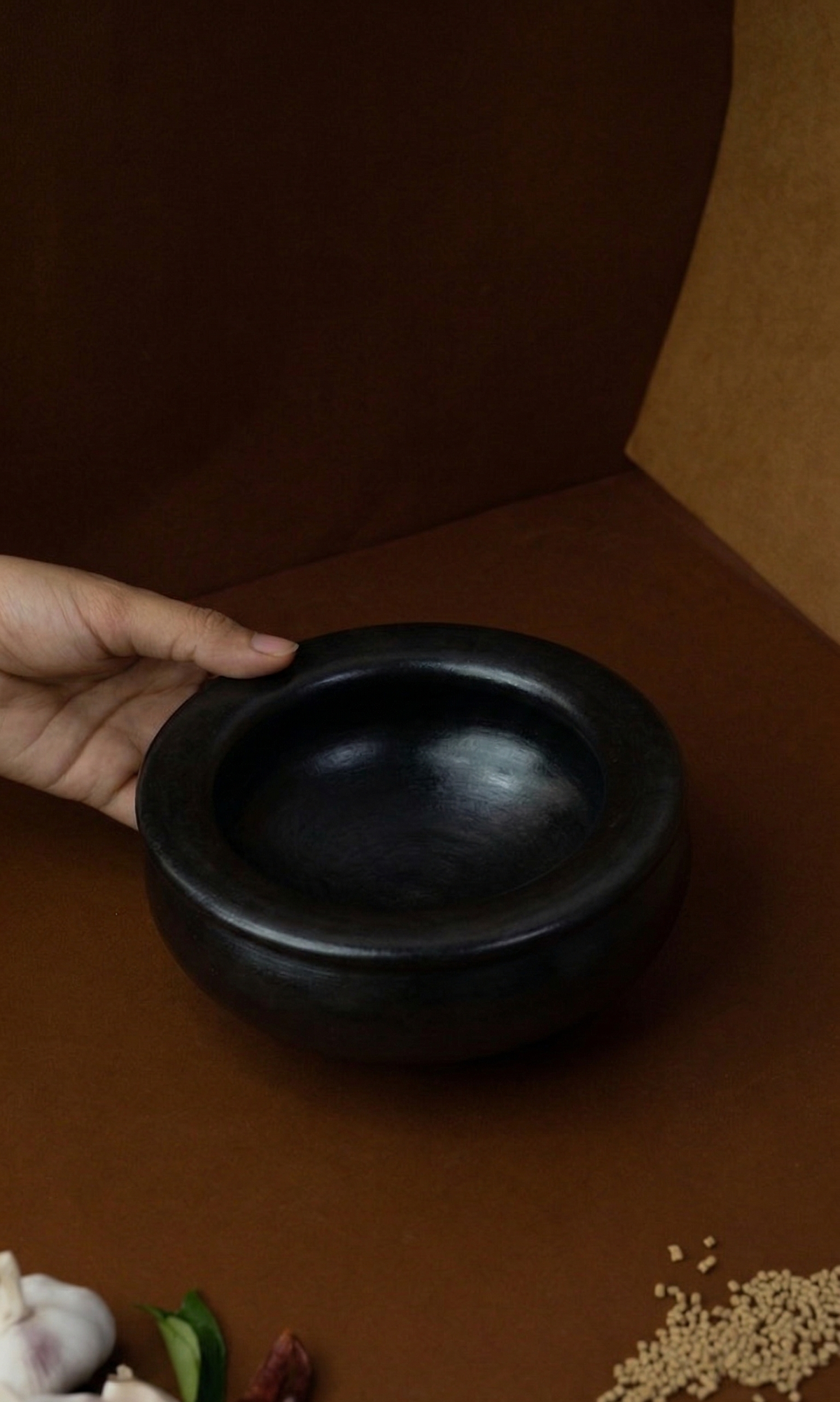 Black Seasoned Uruli Kalchatty held by a hand on a brown surface