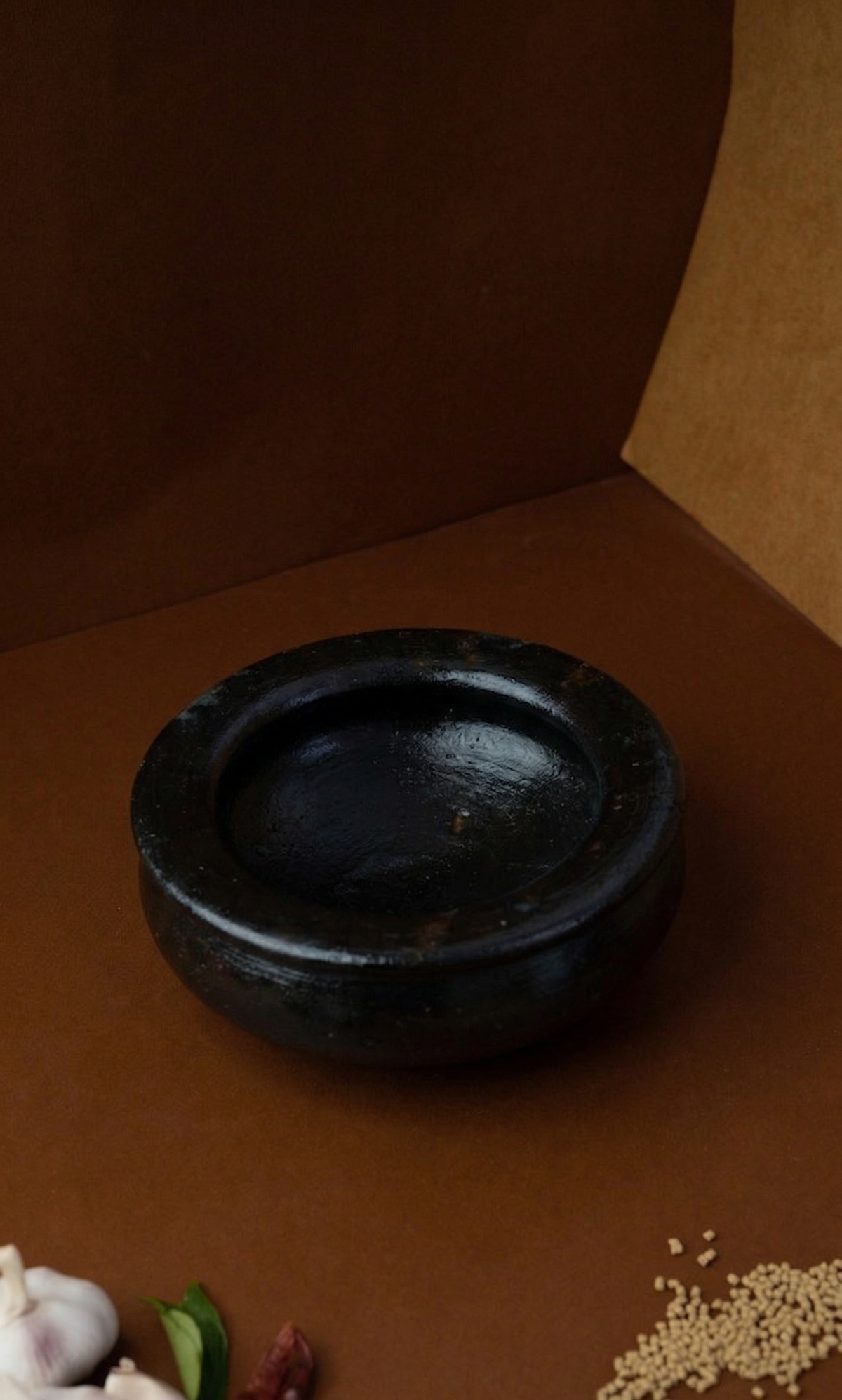 Black Seasoned Uruli Kalchatty on a brown surface with decorative elements.