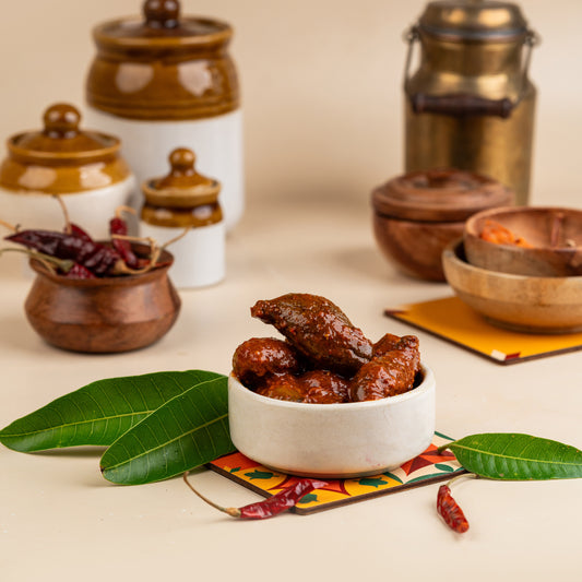 A bowl of pickled mangoes on a colorful cloth, with a background of spice jars and a metal pot.