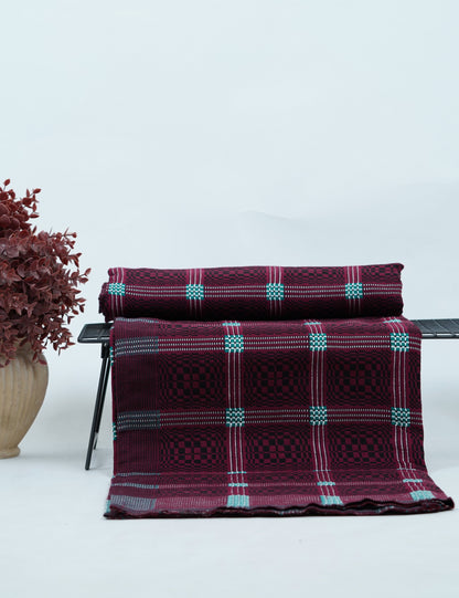 Maroon Nadhiya Chennimalai Bedsheet on a chair with a vase of dried flowers on a light background