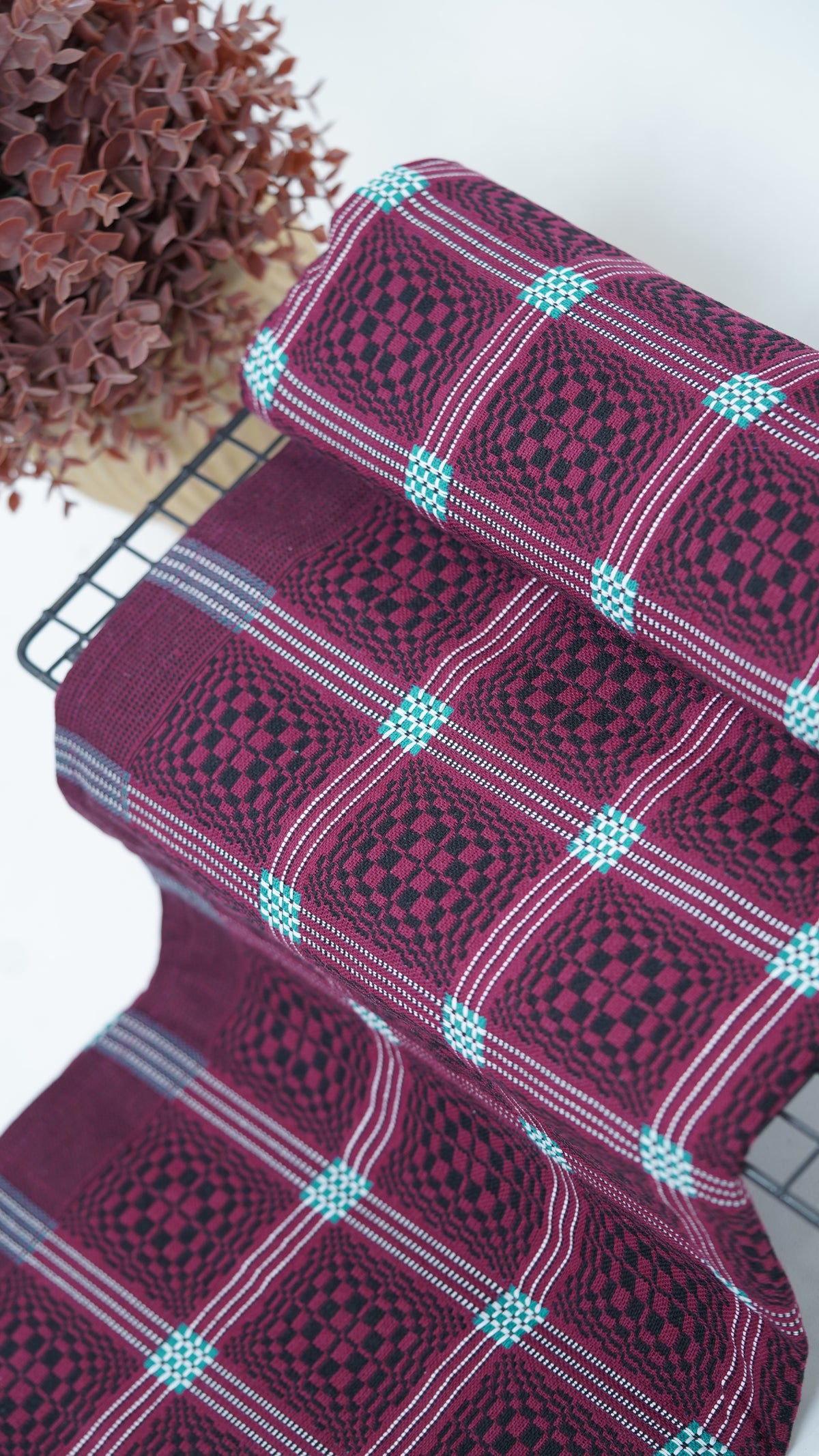 Maroon Nadhiya Chennimalai Bedsheet with a vase of dried flowers on a light background