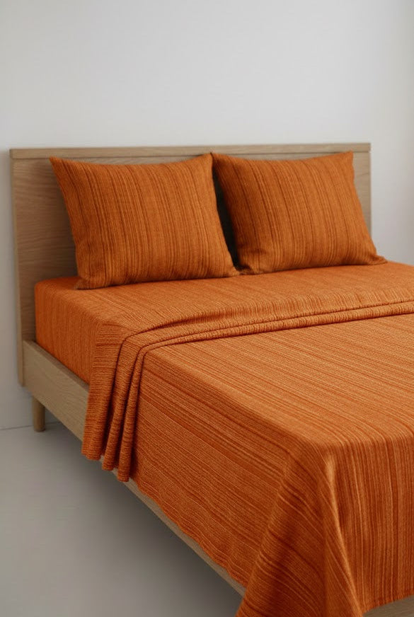 Chennimalai Bedspread Orange textured and pillows on a bed with a wooden headboard.