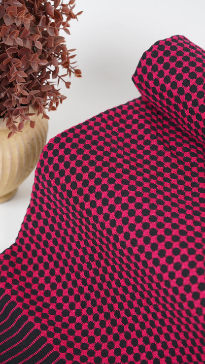 Close-up of a red and black checkered fabric with a plant in the background