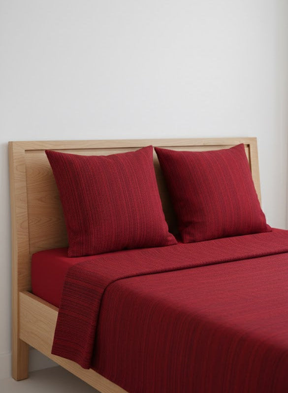 Maroon textured single cot chennimalai bedspread and pillows on a wooden bed against a white wall