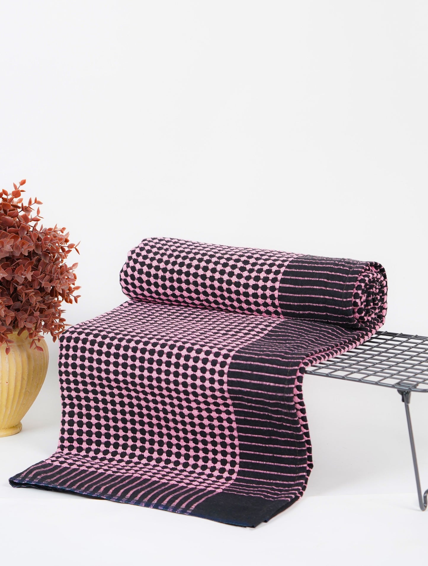 Folded checkered blanket on a chair with a vase of dried flowers on a white background